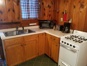 Una cocina con armarios de madera, un lavamanos de acero inoxidable, un microondas, un tostador, una estufa a gas y una cafetera.