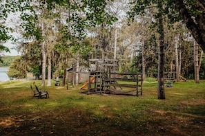 A playground with a slide and climbing structures surrounded by trees and grass.