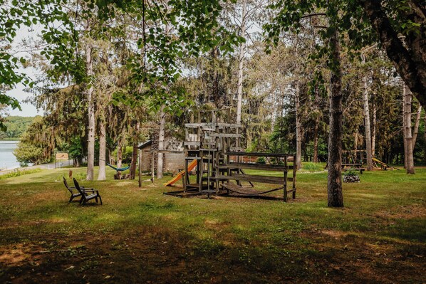 A playground with a slide and climbing structures surrounded by trees and grass.