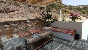 A covered outdoor seating area with a stone wall, a bench, a table with a tray, and a potted plant.