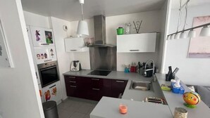 A compact kitchen with a stove, sink, and a small island. There are cabinets above the counter and a trash bin to the left. - Appartement F4 Proche du Stade de France (Saint-Denis)