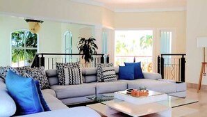 A modern living room with a grey sofa, patterned cushions, a coffee table, and a large potted plant. - 5-bedroom villa in PuntaCana with AC, WiFi, walking distance to white sand beach (Punta Cana)