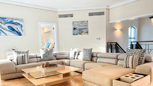 A modern living room with a sectional sofa, a glass coffee table, and artwork on the walls. - 5-bedroom villa in PuntaCana with AC, WiFi, walking distance to white sand beach (Punta Cana)