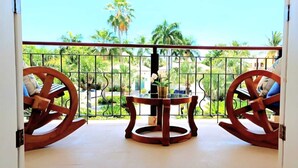 A balcony with two wooden rocking chairs and a small table, overlooking a lush garden with palm trees. - 5-bedroom villa in PuntaCana with AC, WiFi, walking distance to white sand beach (Punta Cana)
