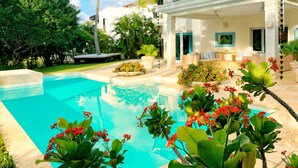 A poolside view of a house with a large pool, surrounded by lush greenery and a well-maintained lawn. - 5-bedroom villa in PuntaCana with AC, WiFi, walking distance to white sand beach (Punta Cana)