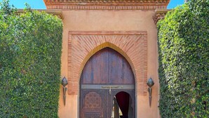 A traditional entrance with a large wooden door, flanked by two elephant statues, leading to a tiled courtyard.