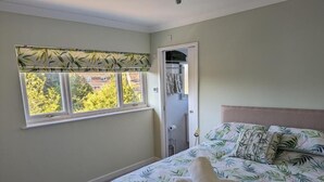 A bedroom with a bed, a window with a leaf-patterned valance, and a door leading to a bathroom. - Little Barham B&B (Braintree)