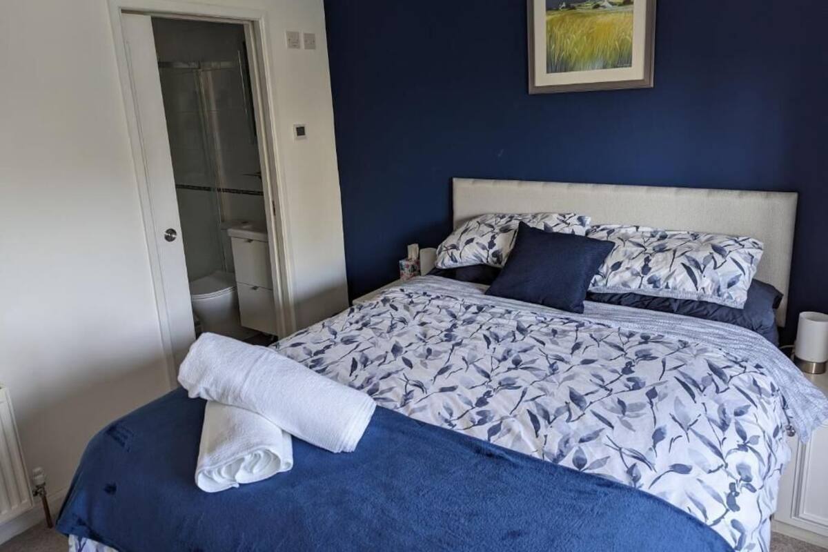 A bedroom with a bed, a nightstand, a painting on the wall, and a door to a bathroom.
