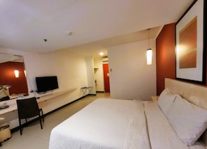 A hotel room with a bed, a desk, a chair, a television, and a wall-mounted artwork. - NamRoom.id Hotel at Glodok Plaza (Jakarta)