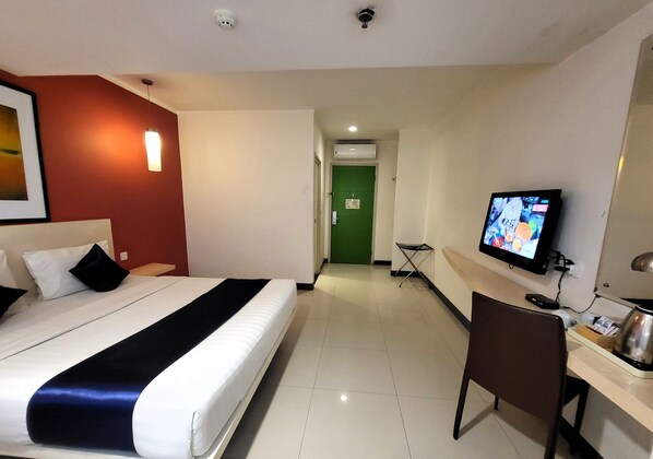 Een hotelkamer met een bed, een bureau, een stoel, een televisie en een groene deur op de achtergrond.