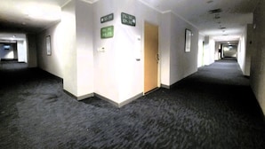 Un couloir d’hôtel avec des panneaux indicateurs, un revêtement de sol en moquette et une porte.