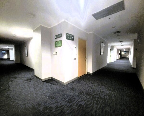 A hotel corridor with directional signs, carpeted floors, and a door. - NamRoom.id Hotel at Glodok Plaza (Jakarta)