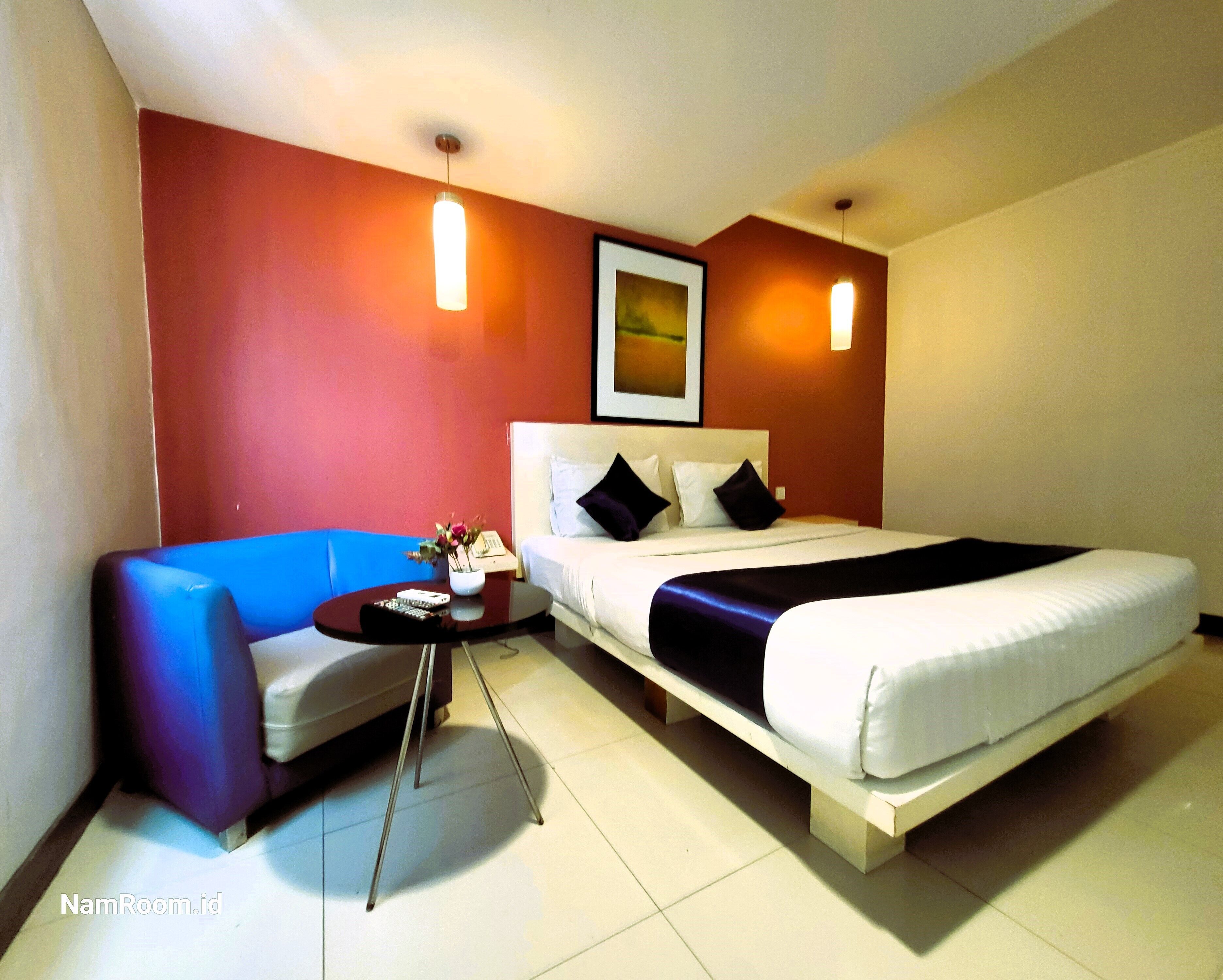 Una habitación de hotel con una cama, un sofá, una mesita con un florero y dos lámparas de pared.