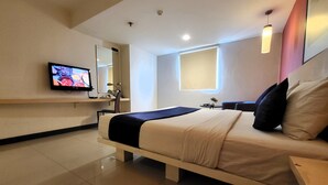 Une chambre d’hôtel moderne dotée d’un grand lit, d’un téléviseur fixé au mur et d’une fenêtre laissant entrer la lumière naturelle.