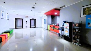 Un hall d’entrée spacieux comprenant un comptoir d’accueil, des distributeurs automatiques et un espace détente avec des coussins aux couleurs vives.