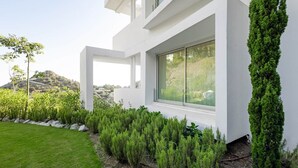 A modern house with a white exterior, large windows, and a well-maintained garden with various shrubs and a tall conifer. - RDR304 - Stunning 2 bedroom Palo Alto, pool, gym + more! (Marbella)