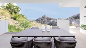 A modern dining area with a table and chairs, overlooking a scenic hillside view. - RDR304 - Stunning 2 bedroom Palo Alto, pool, gym + more! (Marbella)