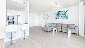 Een ruime woonkamer met een moderne keuken, een grijze bank en een eigentijds kunstwerk aan de muur.