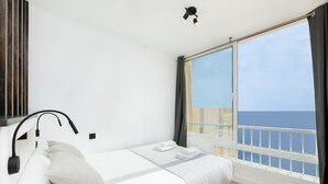 Ett hotellrum med en säng, en sänglampa, ett fönster med utsikt över havet och en balkong.
