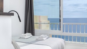 Ett hotellrum med en säng, ett fönster med utsikt över havet och en balkong med ett räcke.