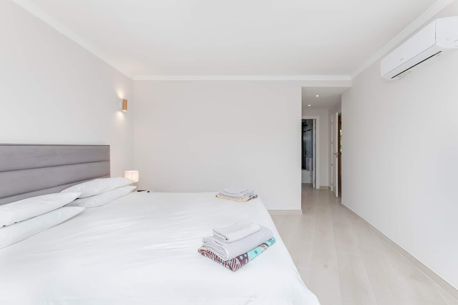 A modern hotel room with a large bed, a bedside table with a lamp, and an air conditioning unit mounted on the wall.