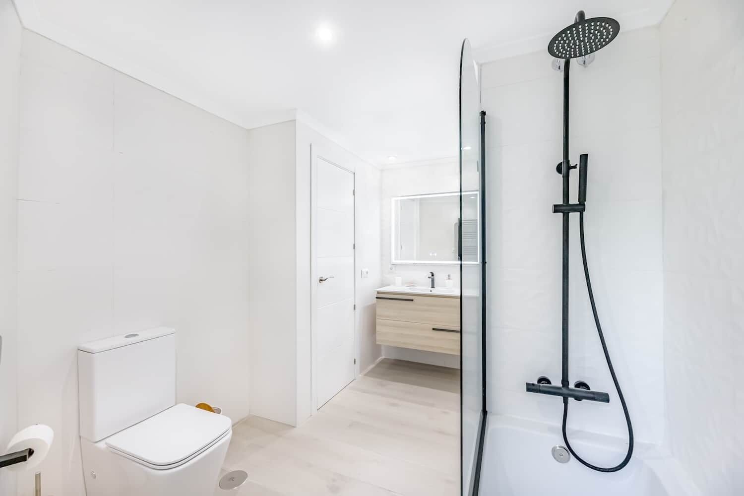 A modern bathroom with a toilet, a shower, and a vanity with a mirror.