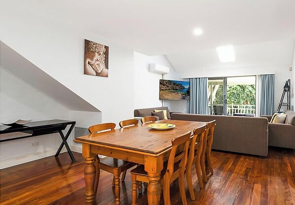 A modern living room with a wooden dining table, a sofa, and a painting on the wall.