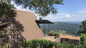 A building with a sloped roof, a covered outdoor area, and a view of a hilly landscape. - The Backyard Blangoda (Balangoda)
