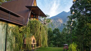 A rustic building with a sloped roof and a stone archway, surrounded by lush greenery and a mountain in the background. - The Backyard Blangoda (Balangoda)