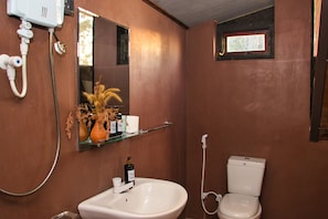 A bathroom with a white sink, a mirror, a toilet, and a shower. - The Backyard Blangoda (Balangoda)