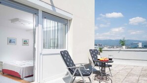 A balcony with a bed, two chairs, a table with fruits, and a city view. - Cozy penthouse with Panoramic view (Zagreb)