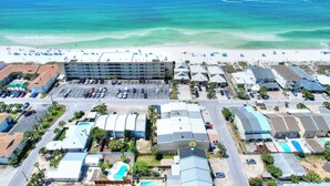 Vue aérienne d’un hôtel situé sur la côte, avec une plage, un parking et plusieurs bâtiments.