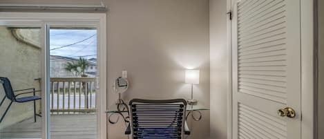 Een kamer met een stoel, een tafel met een lamp, een deur en uitzicht door een glazen deur.