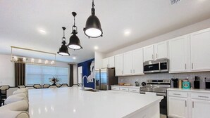 Une cuisine moderne avec des meubles blancs, un grand îlot central, des appareils en acier inoxydable et des luminaires suspendus.