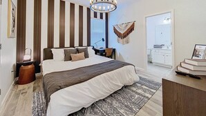 Une chambre moderne avec un grand lit, un lustre, un bureau et une vue sur la salle de bain.