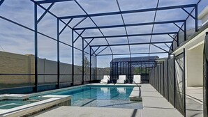 Une piscine dotée d’une zone couverte, entourée d’une structure métallique et de parois en verre, avec un ciel dégagé au-dessus.
