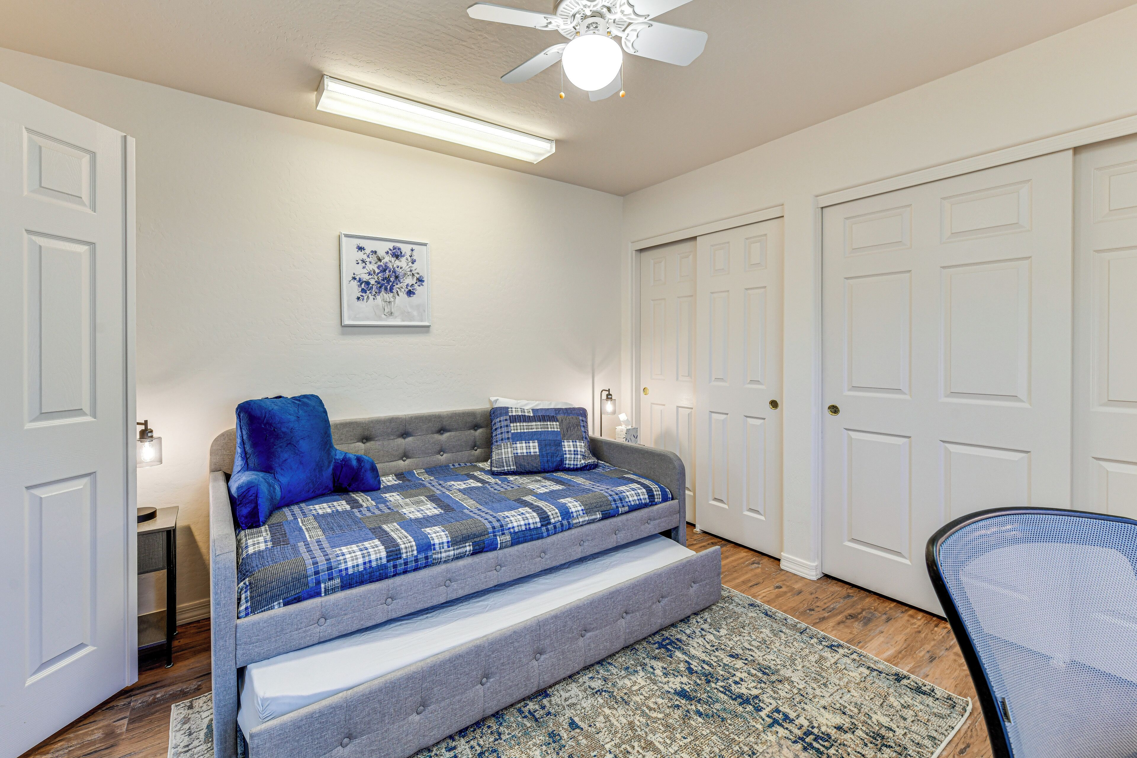 A bedroom with a bed, a chair, a ceiling fan, and a door.