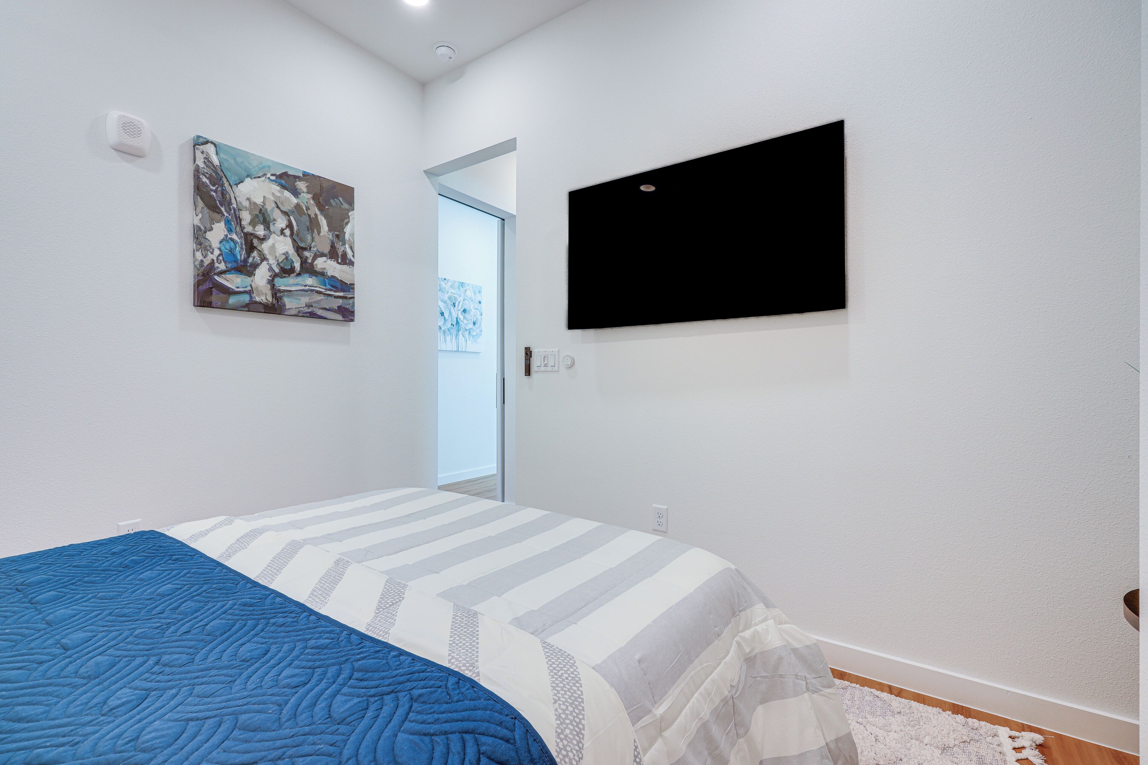 A bedroom with a bed, a painting, a television, and a door leading to another room.