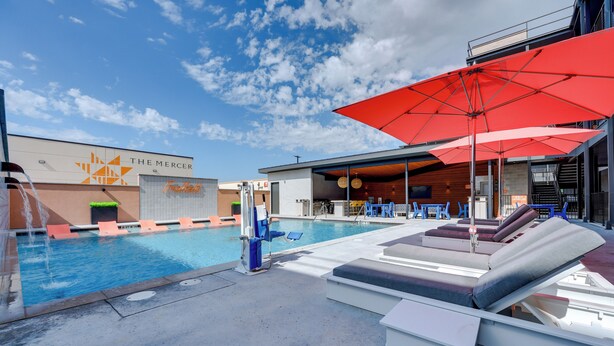 Un espace piscine avec des chaises longues, un parasol rouge et un bâtiment portant l’inscription « THE MERCER ».