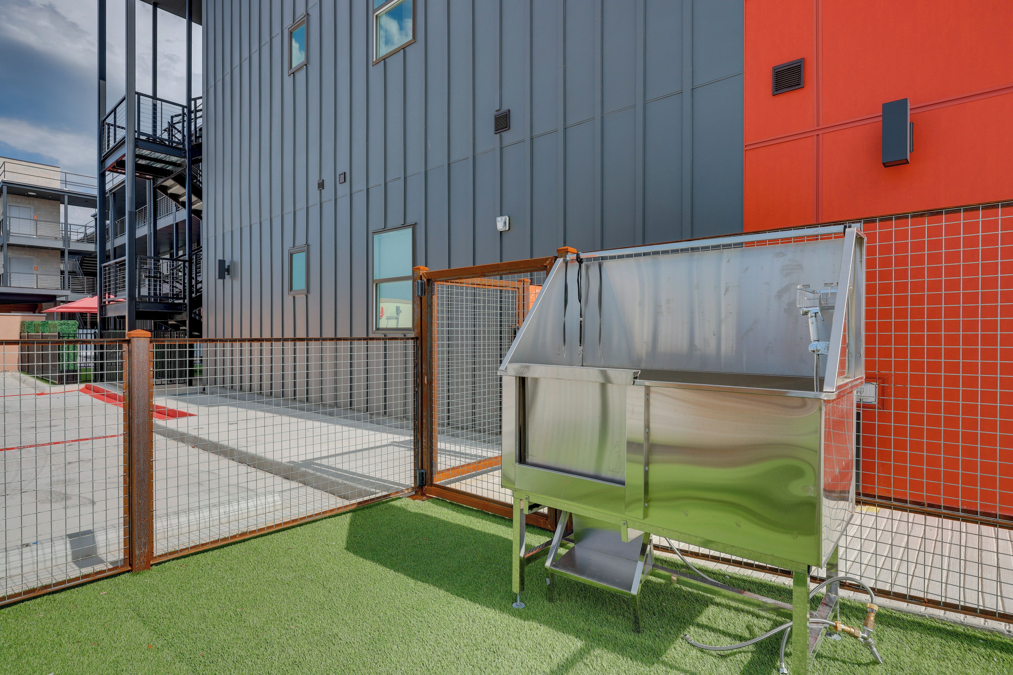 A commercial kitchen with a stainless steel sink and a fenced outdoor area with artificial grass.