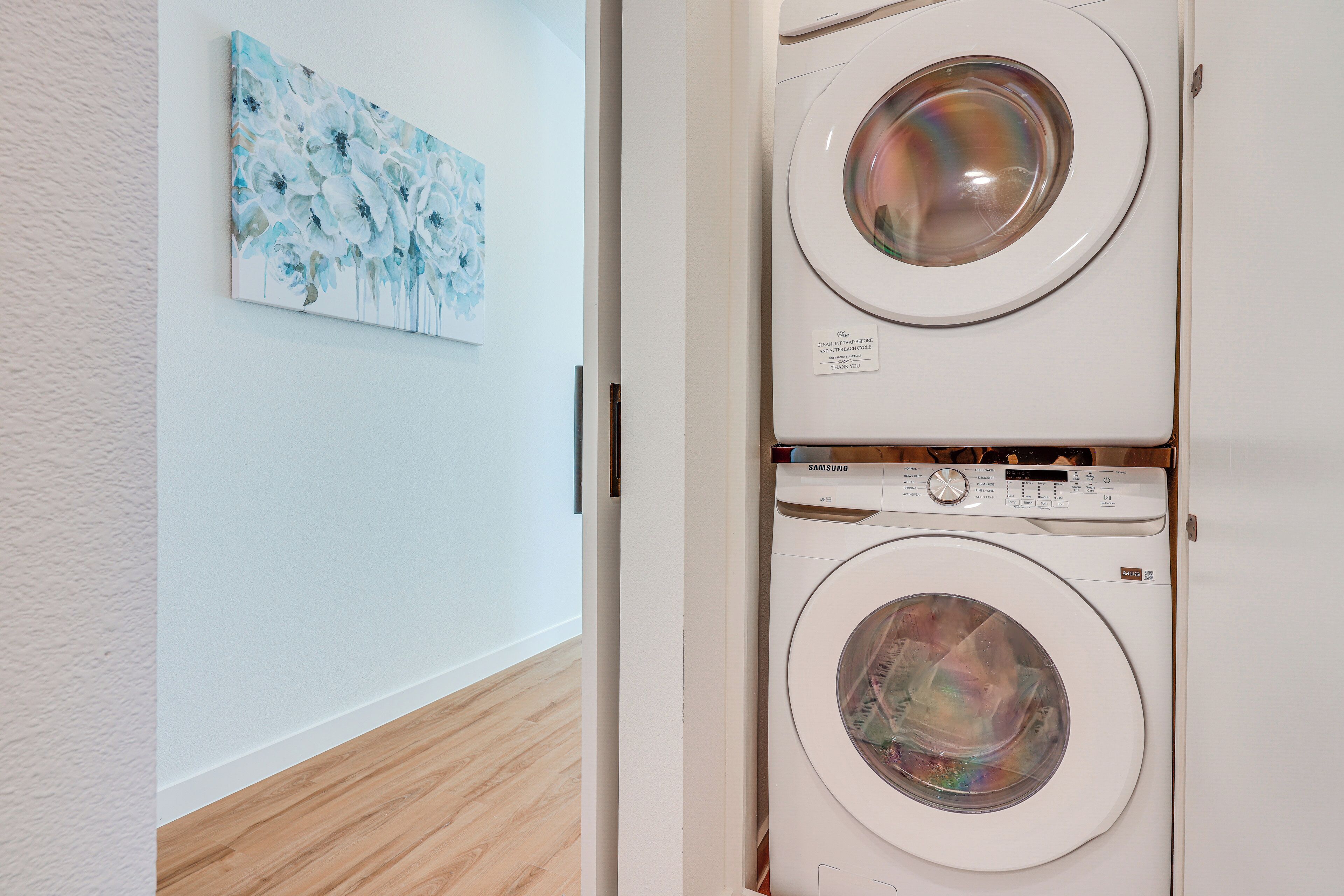 A laundry room with two stacked front-loading washing machines and a wall-mounted painting.