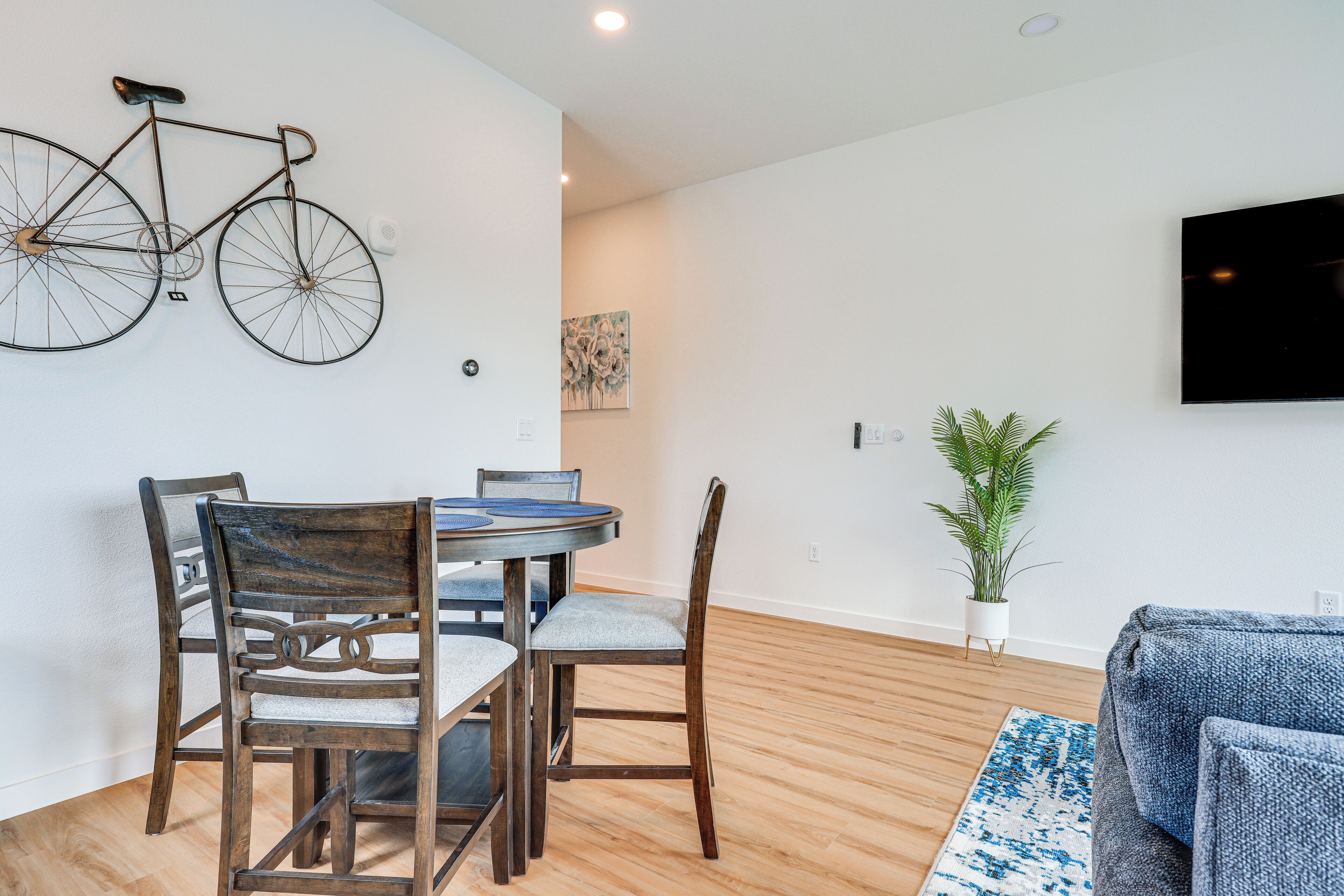 A modern living room with a dining area, wooden flooring, a mounted television, and a potted plant.