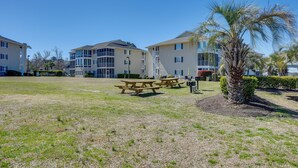 A residential complex with multiple apartment buildings, a grassy lawn, and a palm tree. - Walk to Beach: North Myrtle Beach Condo w/ Sunroom (North Myrtle Beach)