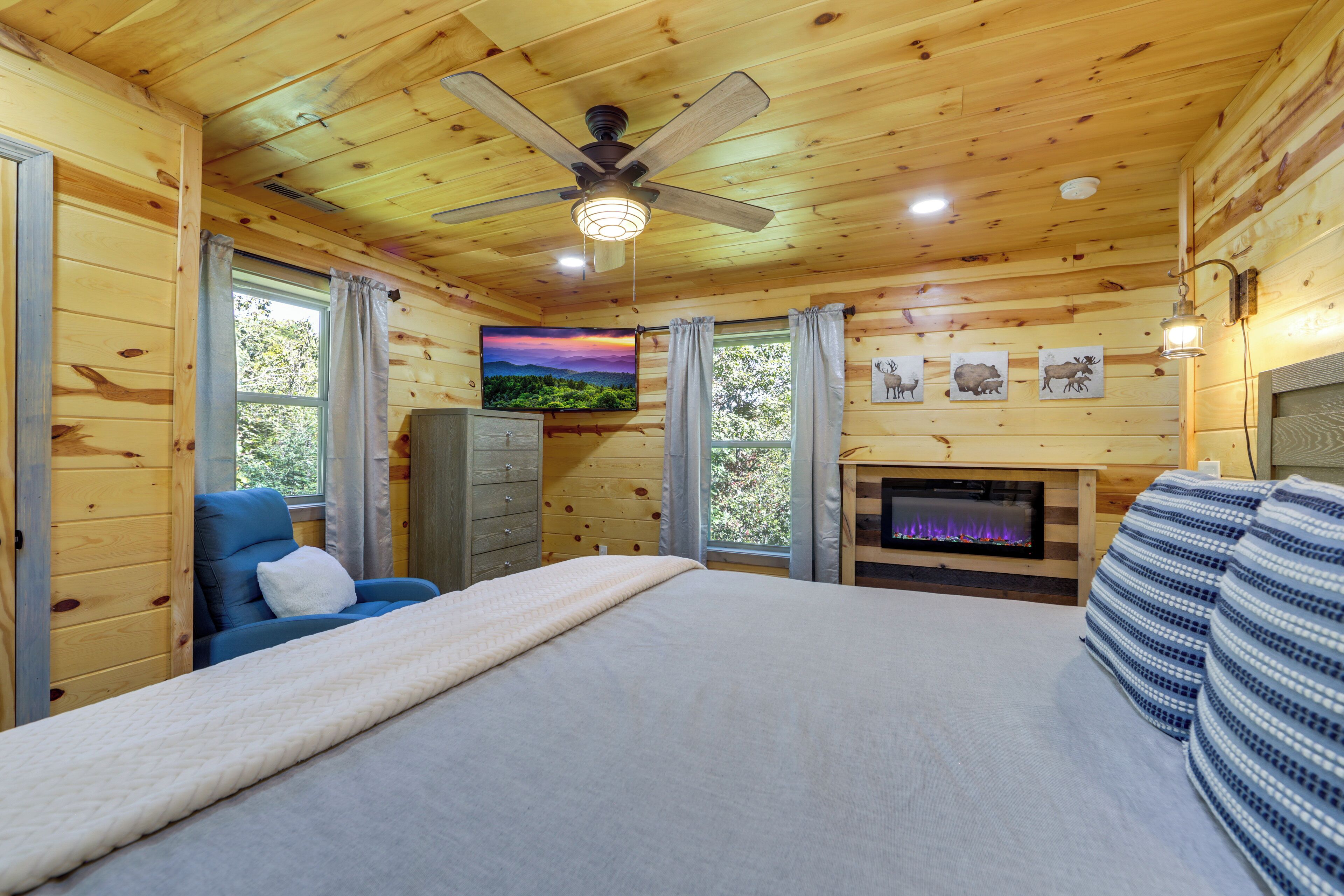 Une pièce de style cabane en bois, avec un lit, une chaise bleue, une cheminée et un téléviseur.