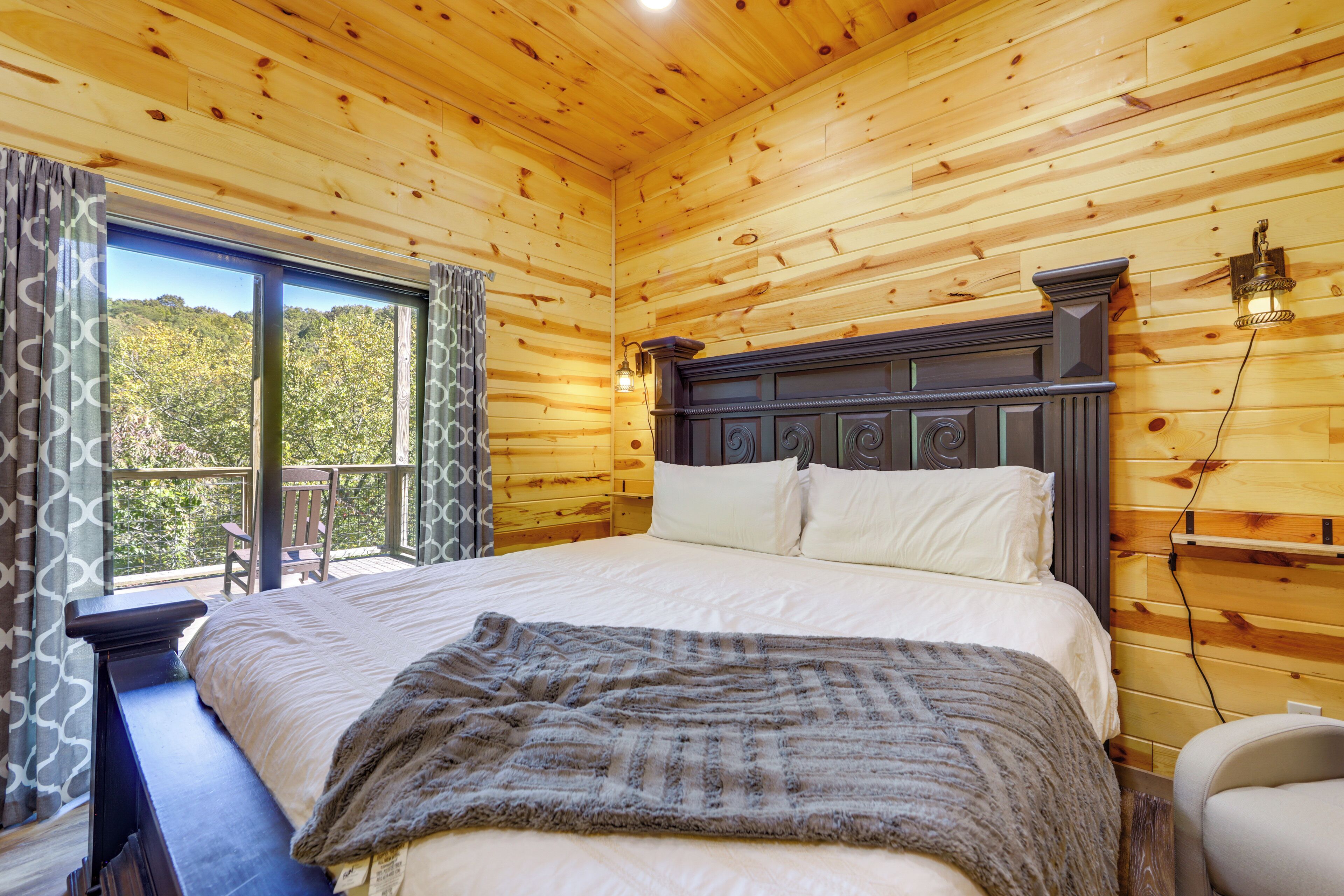 A wooden cabin bedroom with a large bed, a nightstand, a chair, and a window with curtains.