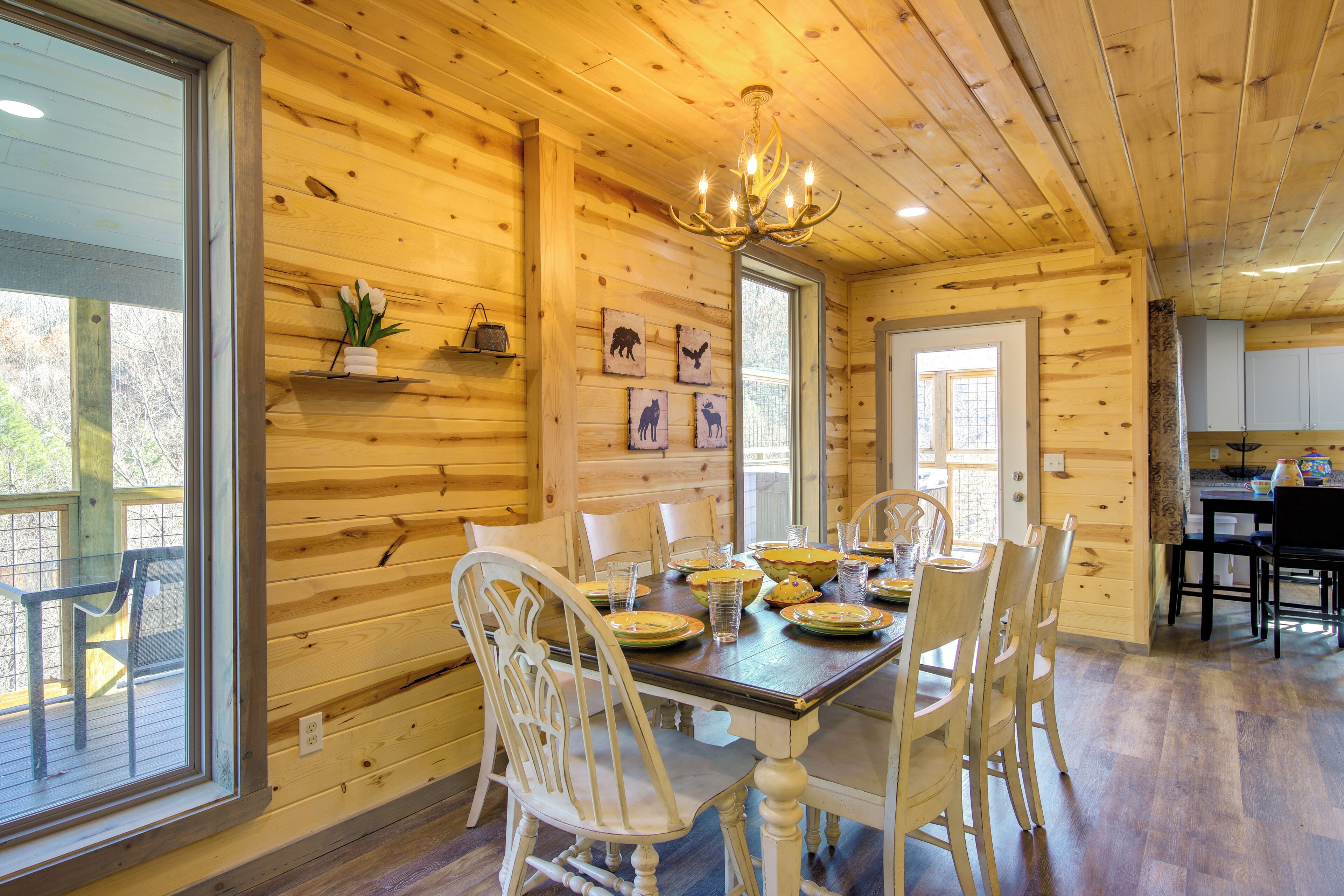 Interior de una cabaña de madera con una mesa de comedor dispuesta para cuatro personas, rodeada de sillas blancas.