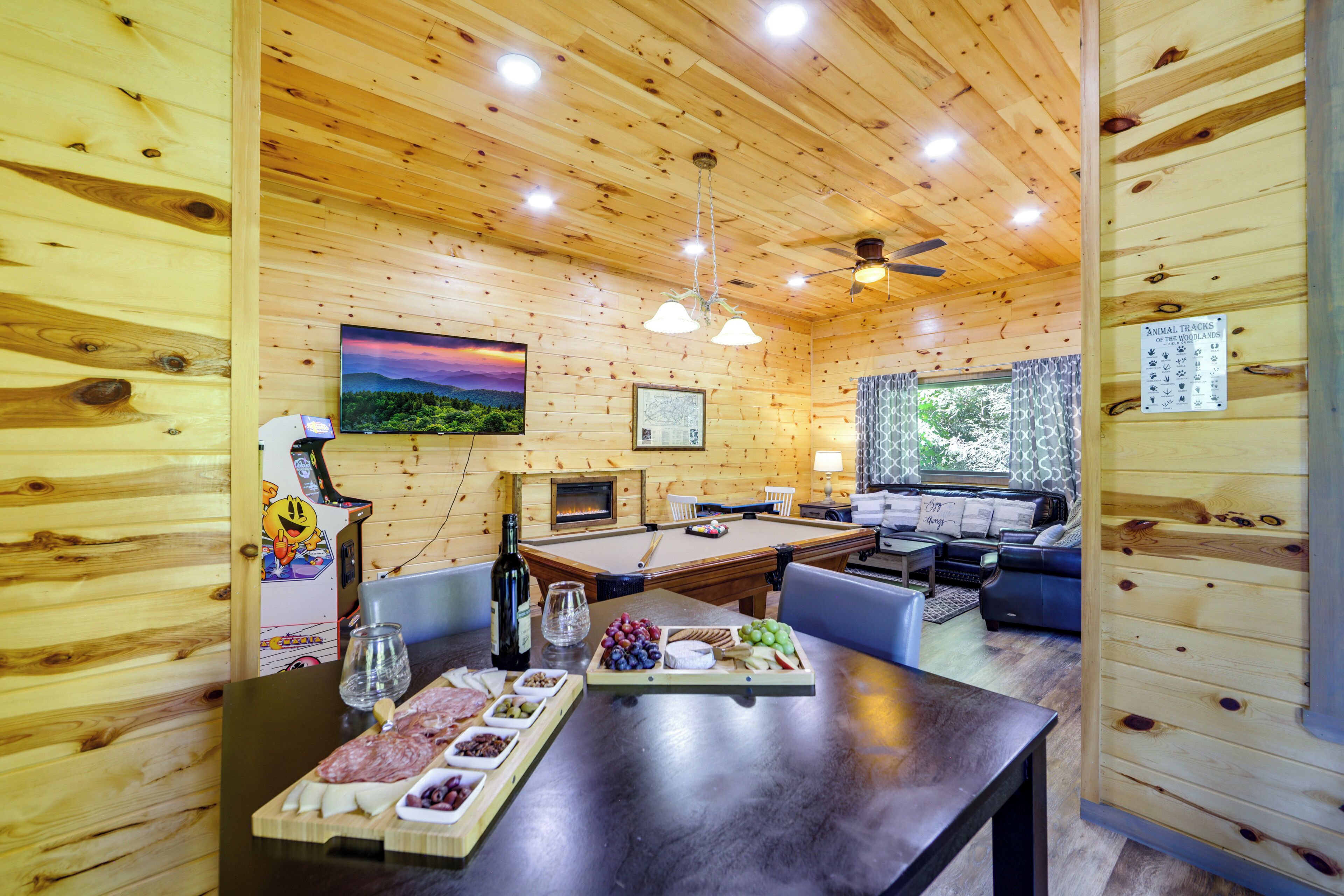 A wooden cabin interior with a pool table, dining table with snacks, and a fireplace.