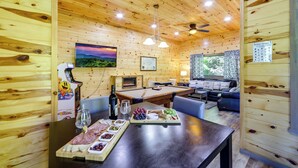 A wooden cabin interior with a pool table, dining table with snacks, and a fireplace.