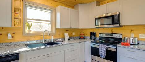 Cozinha moderna com armários brancos, eletrodomésticos de aço inoxidável, bancadas de granito e uma janela que oferece luz natural.