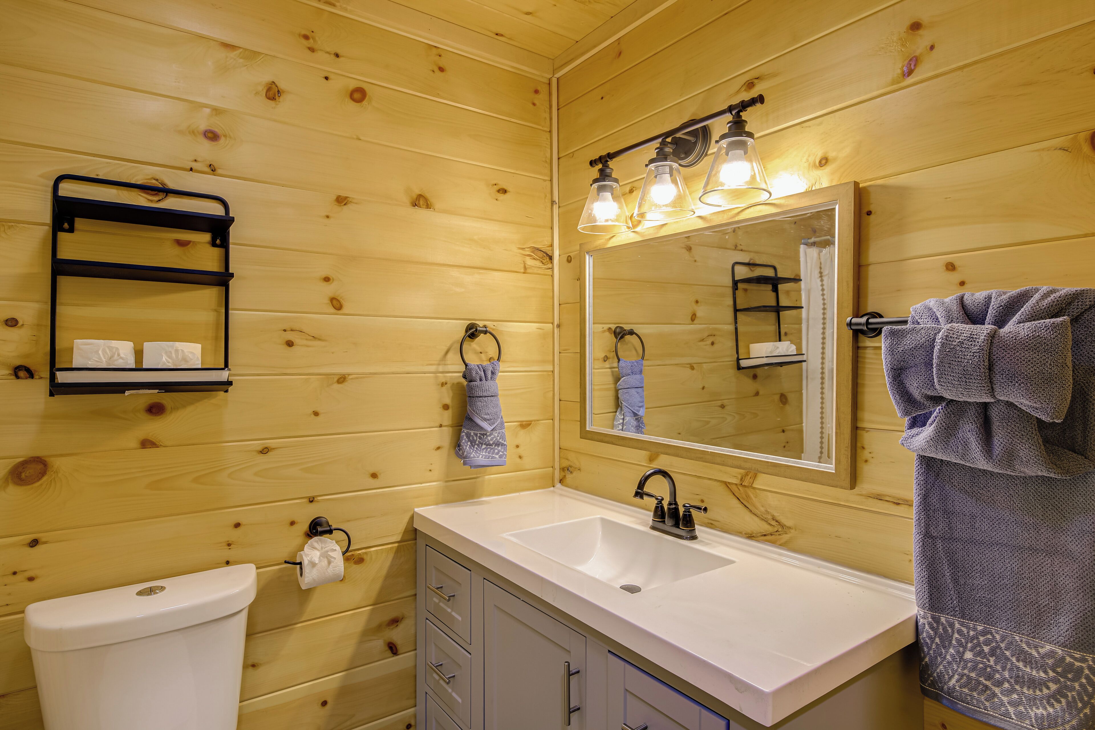 A wooden cabin bathroom with a white sink, a mirror, and a towel rack.